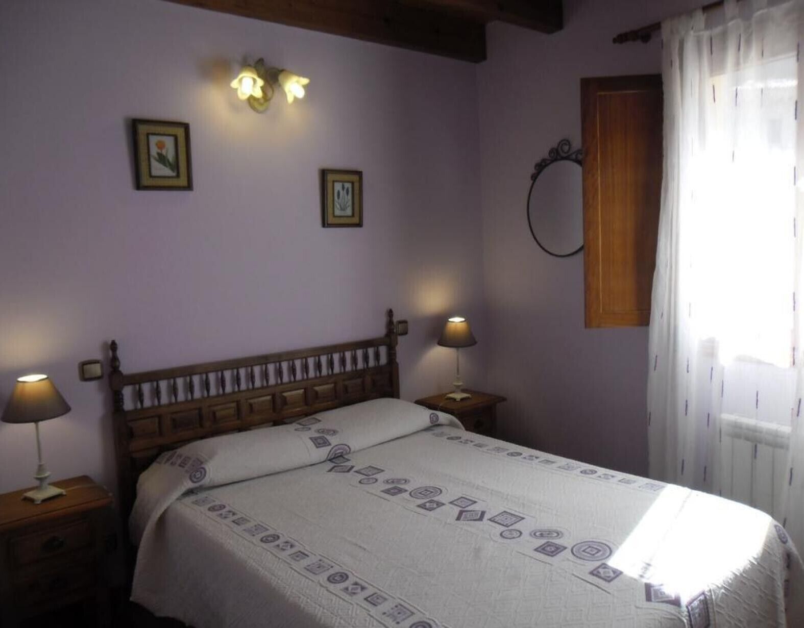 Une chambre à coucher avec un lit en bois, deux lampes de chevet, un luminaire au plafond et une fenêtre avec des rideaux.
