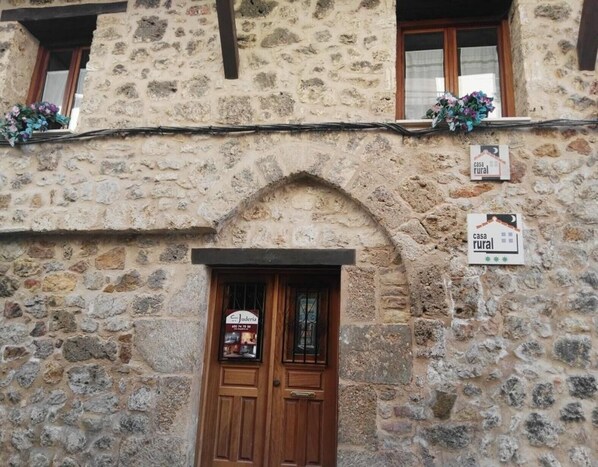 A stone building with a wooden door, a window with a flower box, and a sign indicating a rural house.