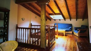 A spacious loft with a high ceiling, wooden beams, a staircase, and a blue sofa.