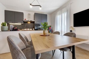 Une cuisine moderne avec des meubles de couleur sombre, une table à manger en bois et un téléviseur à écran plat fixé au mur.