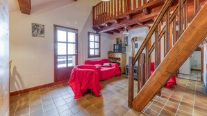 A room with a wooden staircase, two beds with red covers, a window, and a door.