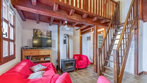 A cozy living room with a red sofa, a television, a fireplace, and a wooden staircase.