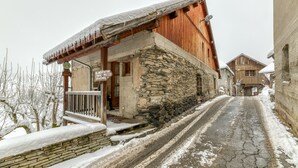 A stone building with a wooden upper floor, a sign indicating a restaurant, and a snow-covered street.