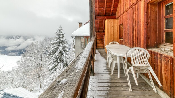 A wooden cabin with a balcony overlooking a snowy landscape.