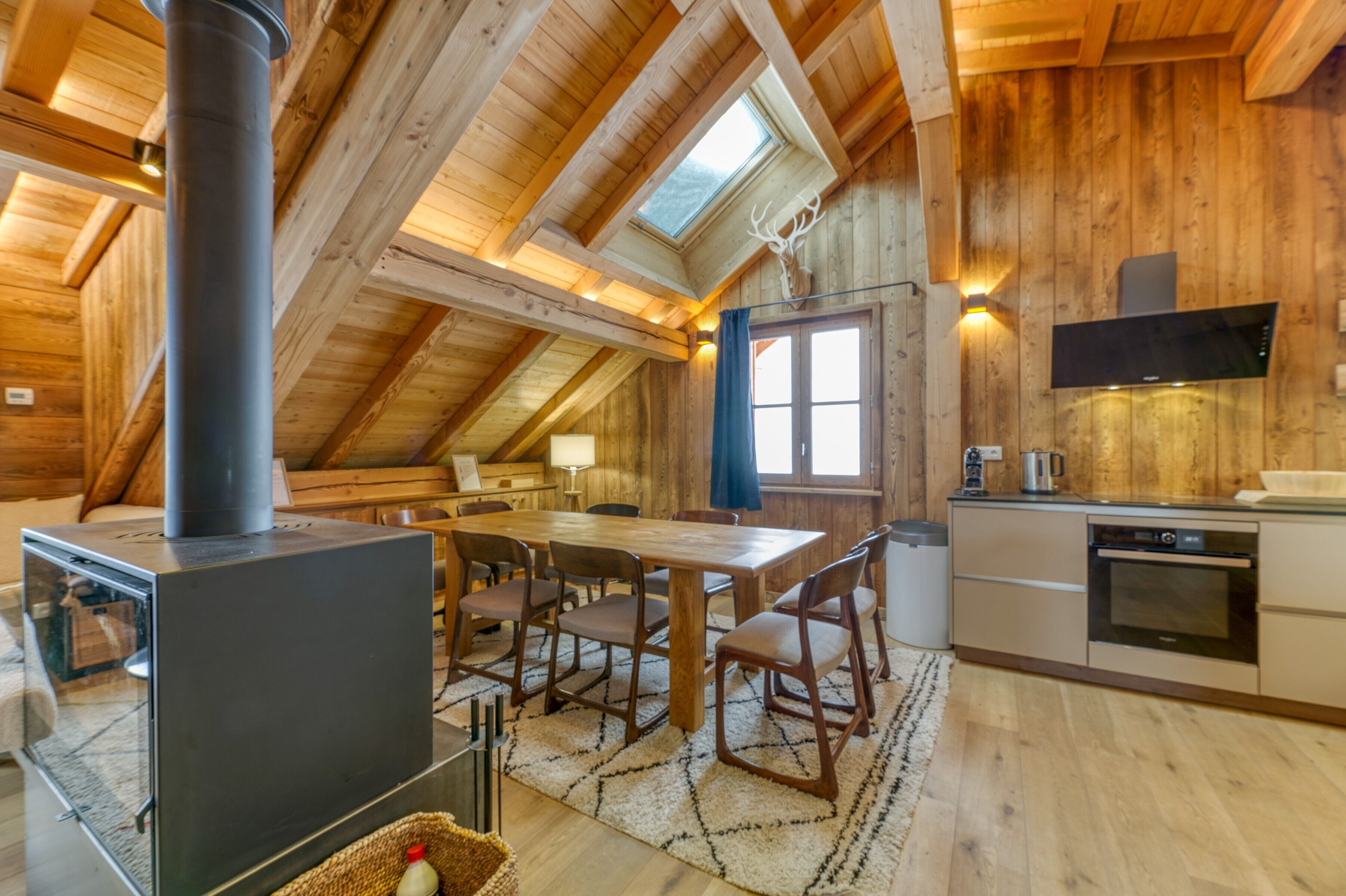 A wooden interior with a dining table, chairs, a stove, and a kitchen area.