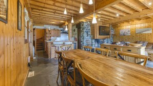 Un interior de madera con una larga mesa de comedor, sillas, lámparas colgantes, detalles de piedra y una zona de cocina.