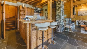Un interior de madera con chimenea de piedra, taburetes de bar de madera y una zona de cocina.