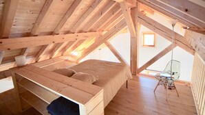 A loft bedroom with a wooden ceiling, a bed, a chair, and a small window. - Chalet '4 Étoiles La Saulire' with Mountain View, Shared Terrace and Wi-Fi (Villard-Reculas)
