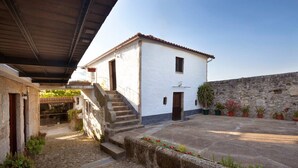 A courtyard with a white building, stone wall, and potted plants. - Apartment 'Casa Do Caldas - Casa 4' with Shared Pool, Wi-Fi and Air Conditioning (Retorta)