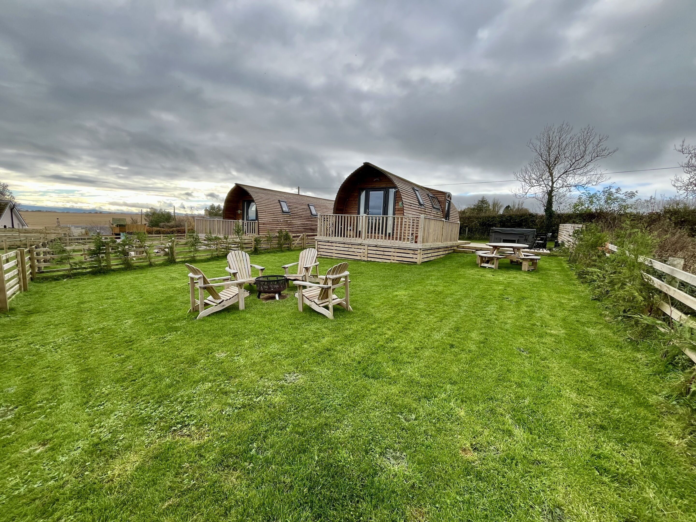 A rustic wooden cabin with a deck, surrounded by a well-maintained lawn and outdoor seating area.
