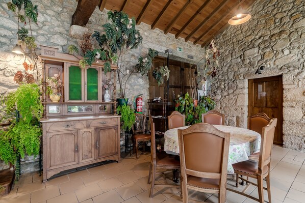 Un intérieur rustique avec un mur en pierres apparentes, une table et des chaises en bois, un meuble avec des portes en verre et diverses plantes en pot.