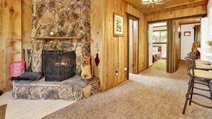A cozy room with a stone fireplace, wooden walls, and a dining area with a bar stool.