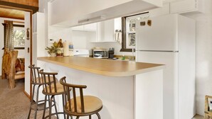 A kitchen with a wooden island, bar stools, a microwave, and a refrigerator.