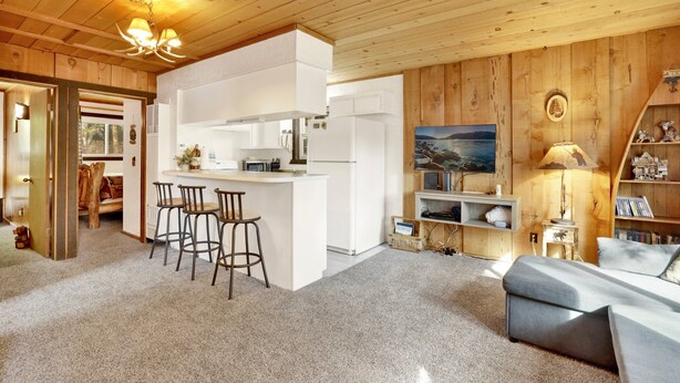 A cozy kitchen with a bar area, wooden walls, and a large window.
