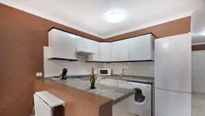 A kitchen with white cabinets, a built-in microwave, a washing machine, and a small bar area with a bottle and glass.
