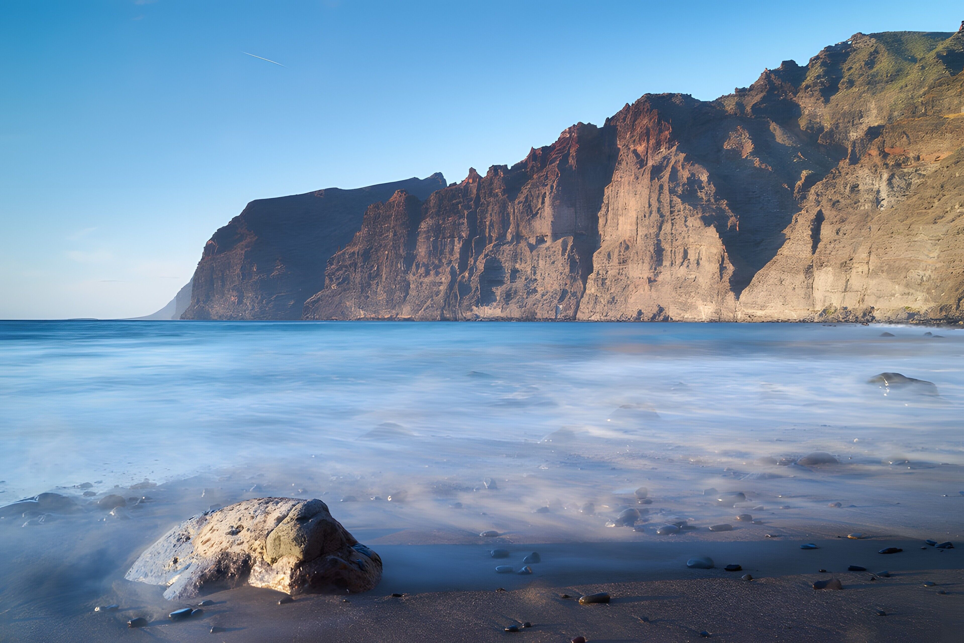 Una playa con una roca grande al frente y un acantilado en el fondo.