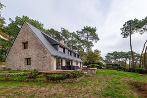 A stone house with a sloped roof, a deck with outdoor seating, and a well-maintained lawn.
