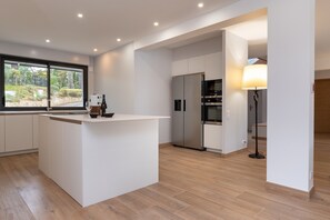 A modern kitchen with a central island, built-in appliances, and a view through a large window.