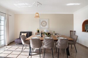 A dining area with a wooden table set for six, surrounded by six chairs, a decorative wall piece, and a hanging light fixture.