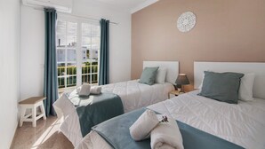 Een hotelkamer met twee bedden, een raam met gordijnen, een klein krukje en een decoratie aan de muur.
