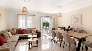 Een moderne woonkamer met een bank, eettafel, stoelen en uitzicht op buiten.