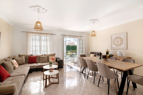 A modern living room with a sofa, dining table, chairs, and a view to the outside.