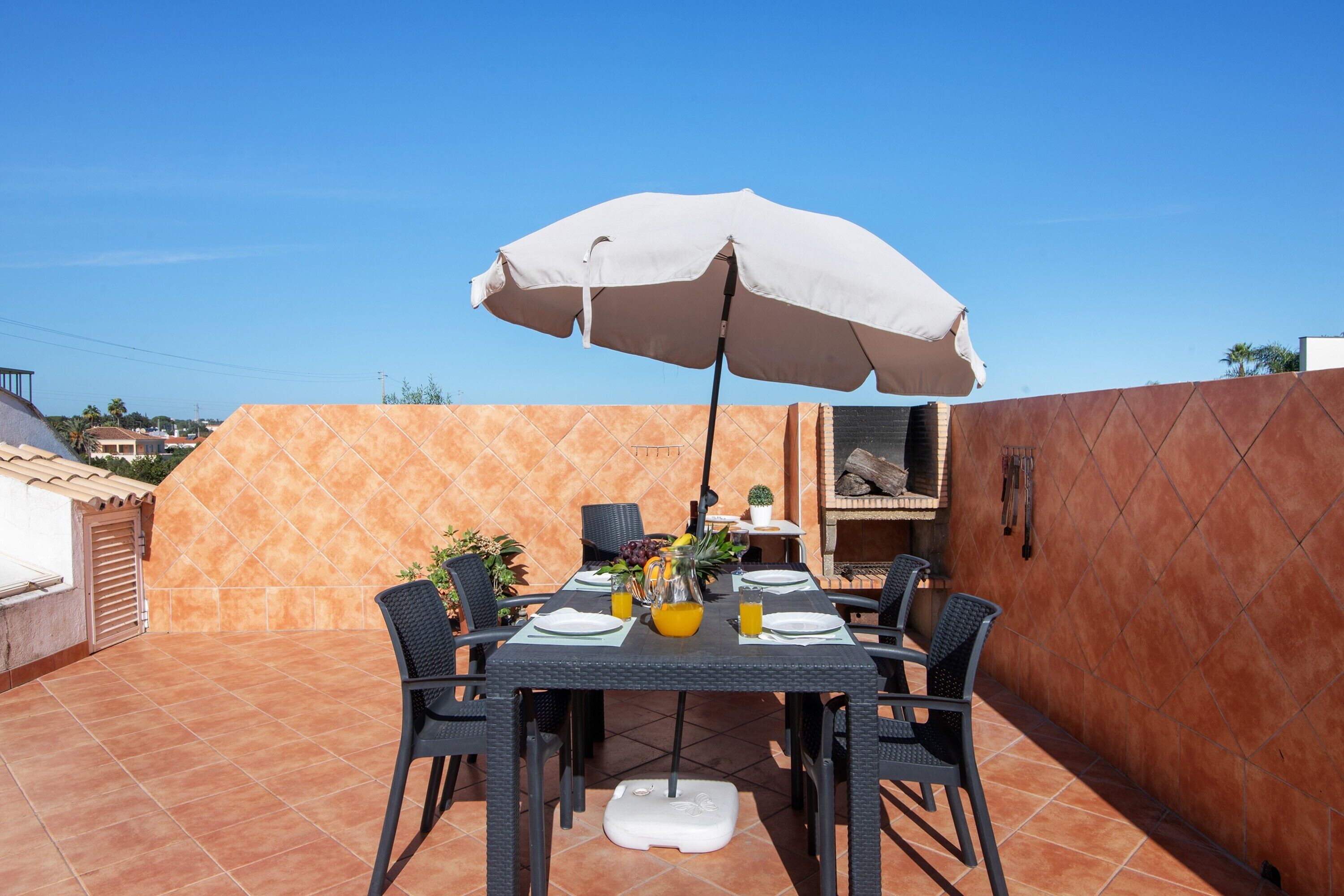 An outdoor patio with a table set for two, a white umbrella, and a small garden area.
