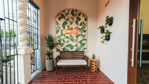 A hallway with a bench, potted plants, and a neon sign.