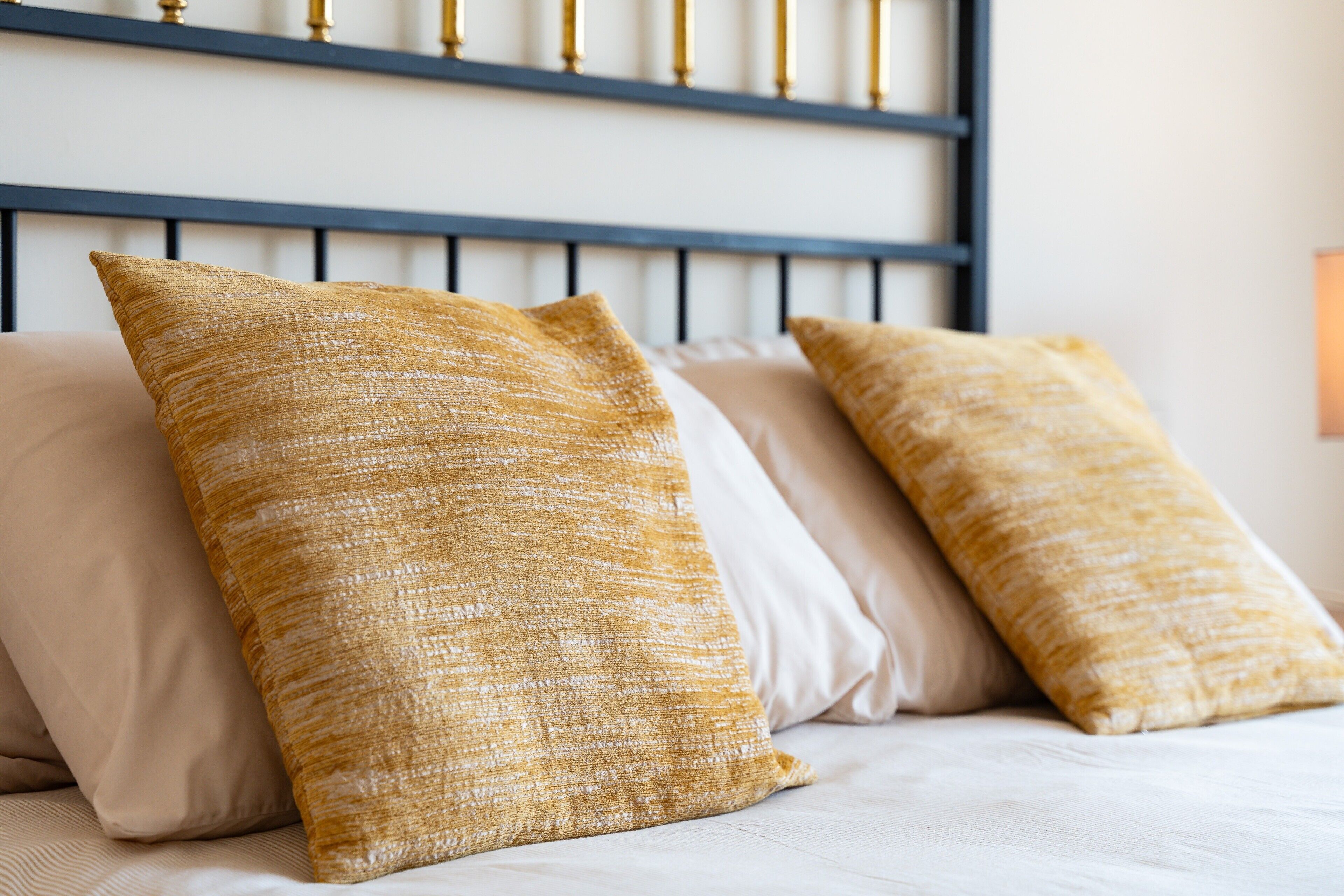 A bed with three pillows, a headboard, and a wall-mounted light fixture.