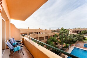 A balcony with two lounge chairs, a pool, and a view of surrounding buildings.