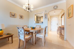 A dining area with a round table, chairs, a chandelier, framed pictures on the wall, and a clock.