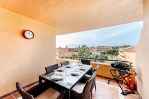 A balcony with a dining table set for four, a clock, and a barbecue grill.