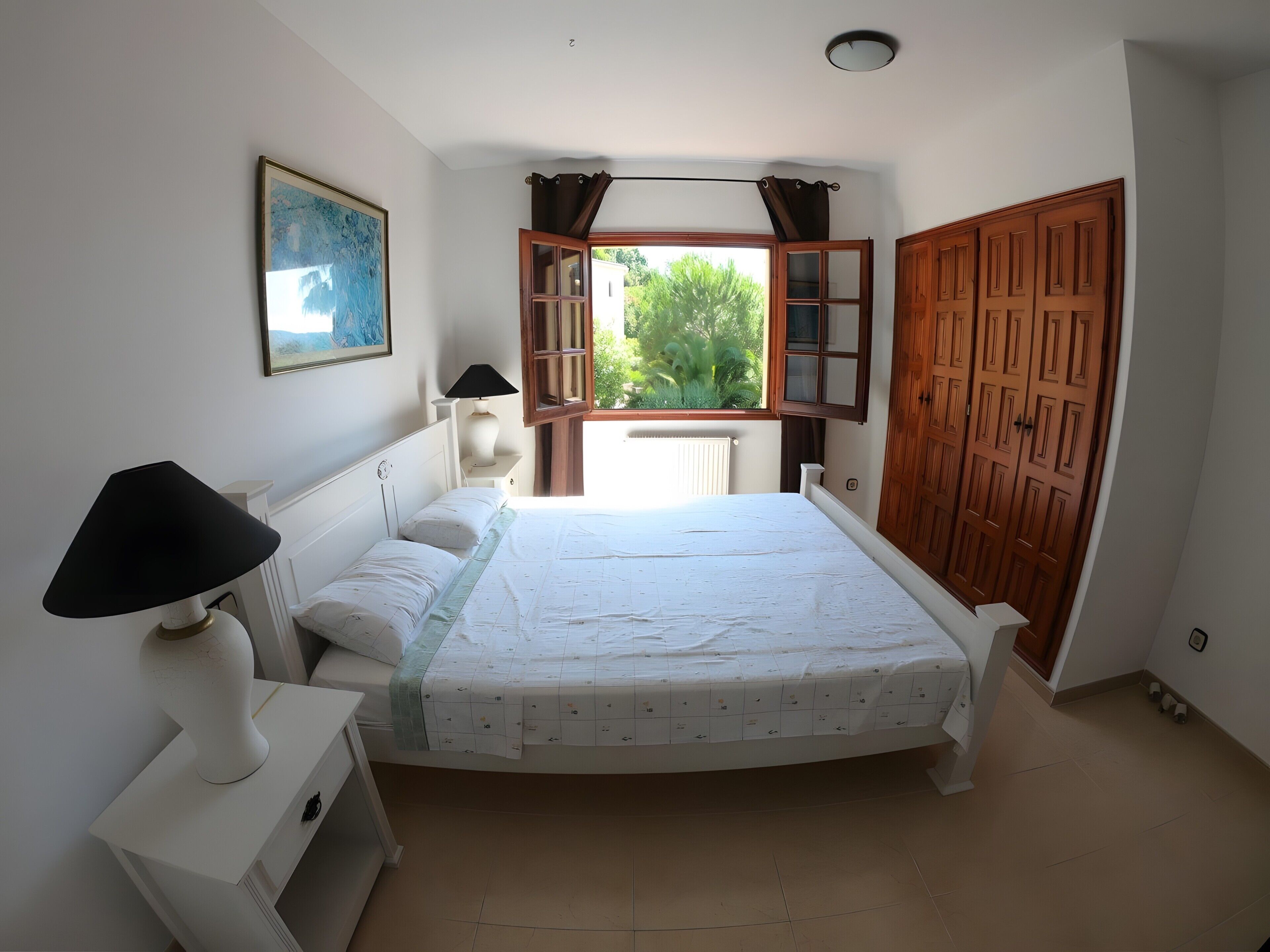 A bedroom with a bed, bedside lamp, nightstand, and a window with curtains.