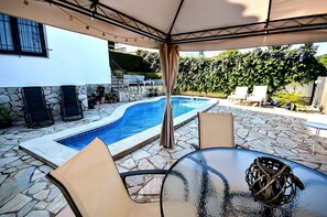 A poolside area with stone flooring, a glass table, and lounge chairs.