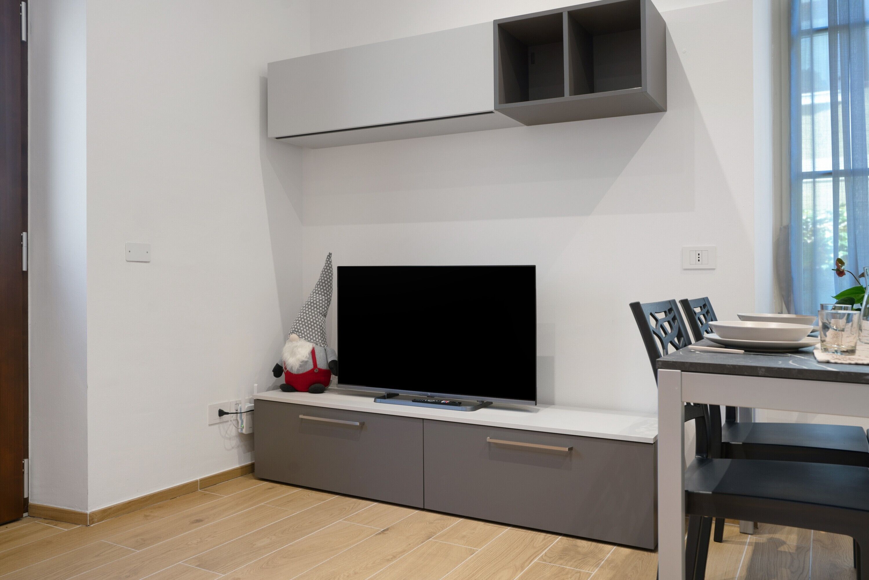 Una sala de estar moderna con un televisor de pantalla plana, gabinetes grises y una zona de comedor con mesa y sillas.