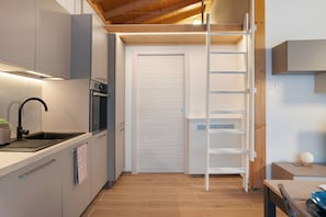 Een compacte keuken met een ingebouwde oven, een spoelbak en een ladder die naar een opbergruimte leidt.