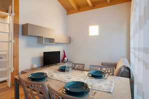 Een eethoek met een tafel gedekt voor vier personen, een televisie en een plank erboven.