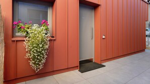 A building with a red exterior, a window with flowers, a door, and a tiled floor. - Apartment 'Appartamento Chiara Tione' with Private Garden and Wi-Fi (Tione di Trento)