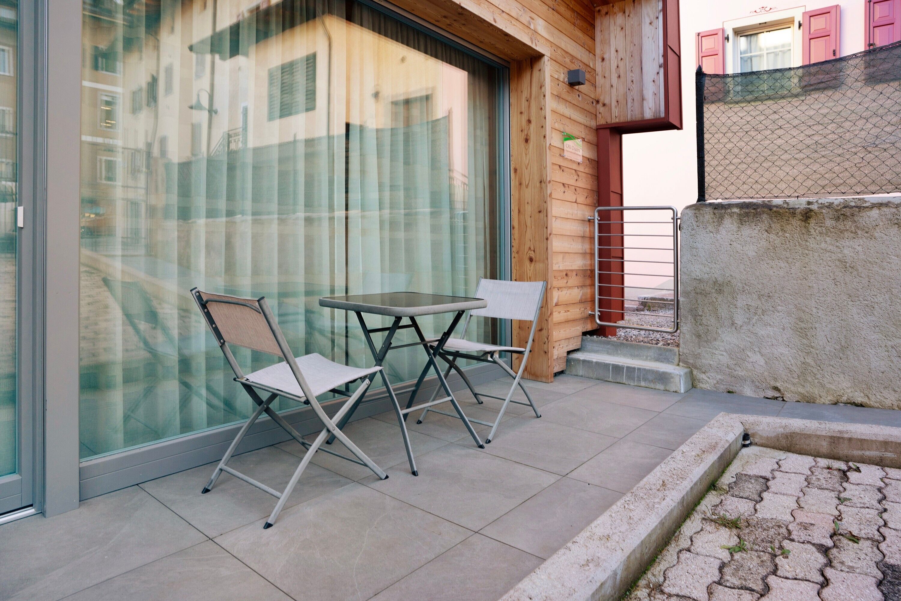 A balcony with a glass door, a small table, two chairs, and a concrete ledge.