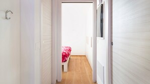 A narrow hallway with a bed at the end, wooden flooring, and white walls. - Apartment 'Appartamento Chiara Tione' with Private Garden and Wi-Fi (Tione di Trento)