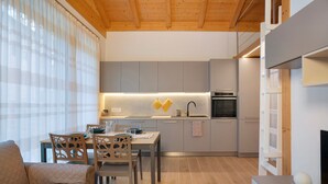 A modern kitchen with grey cabinets, a wooden ceiling, and a dining area with a table and chairs. - Apartment 'Appartamento Chiara Tione' with Private Garden and Wi-Fi (Tione di Trento)