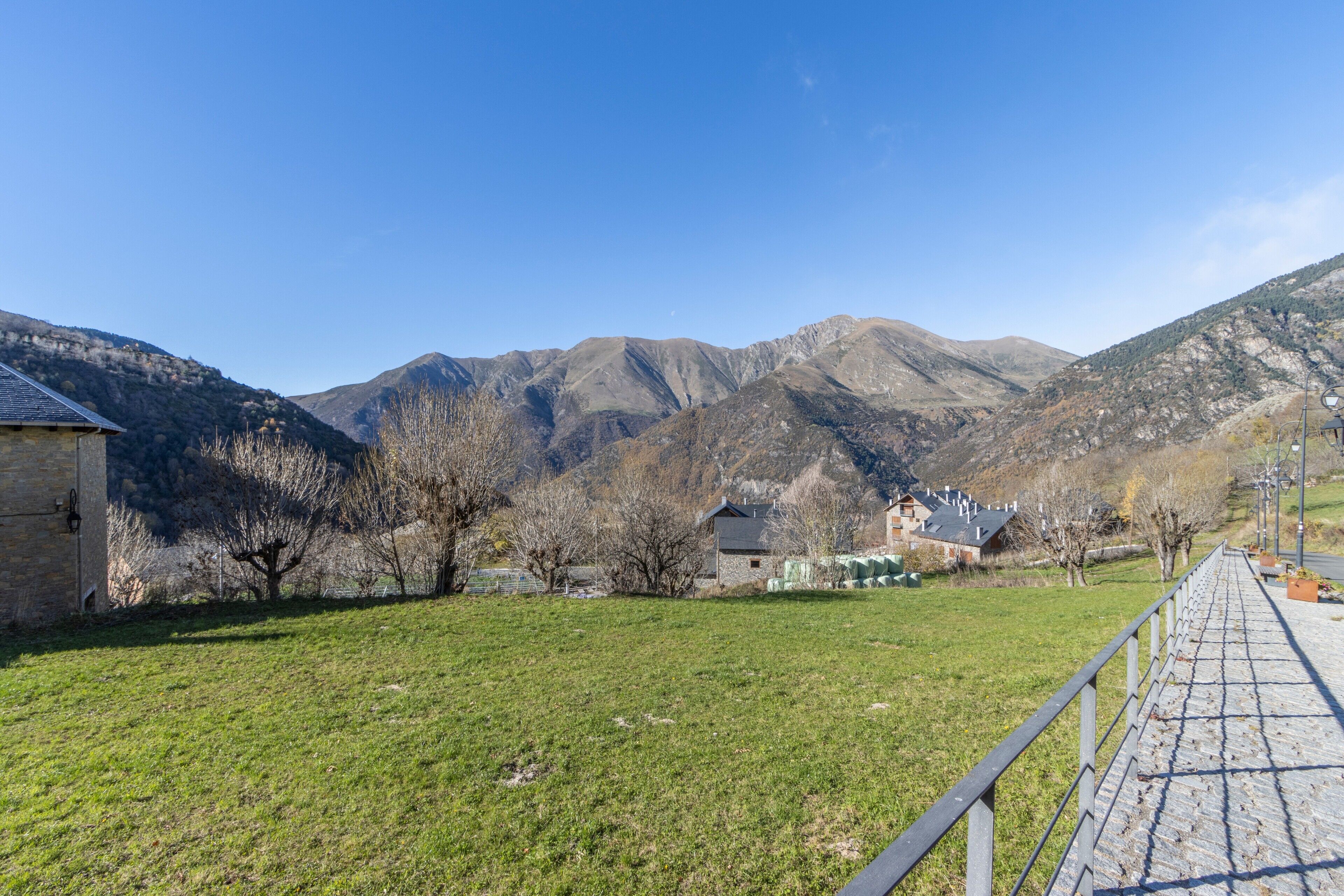 Un edificio de piedra con techo plano, un sendero empedrado y montañas al fondo.