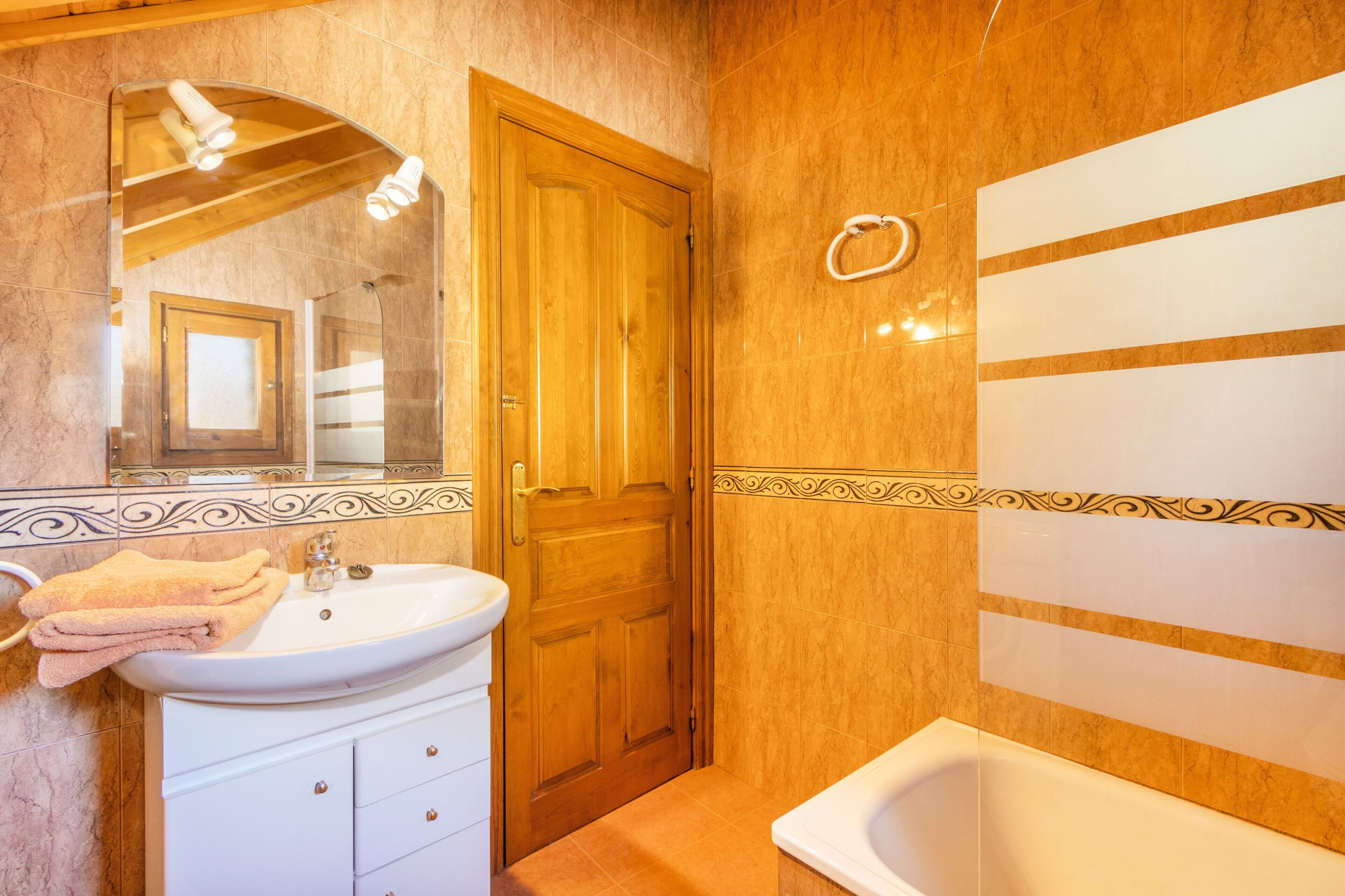 Ein Badezimmer mit Waschbecken, Spiegel, Holztür und Badewanne.