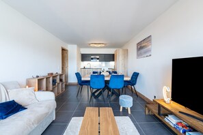 Una sala de estar moderna con un sofá, una mesa de centro y un televisor. Hay una zona de comedor con una mesa y sillas.