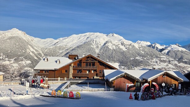 Een houten lodge met balkon, omringd door besneeuwde bergen.