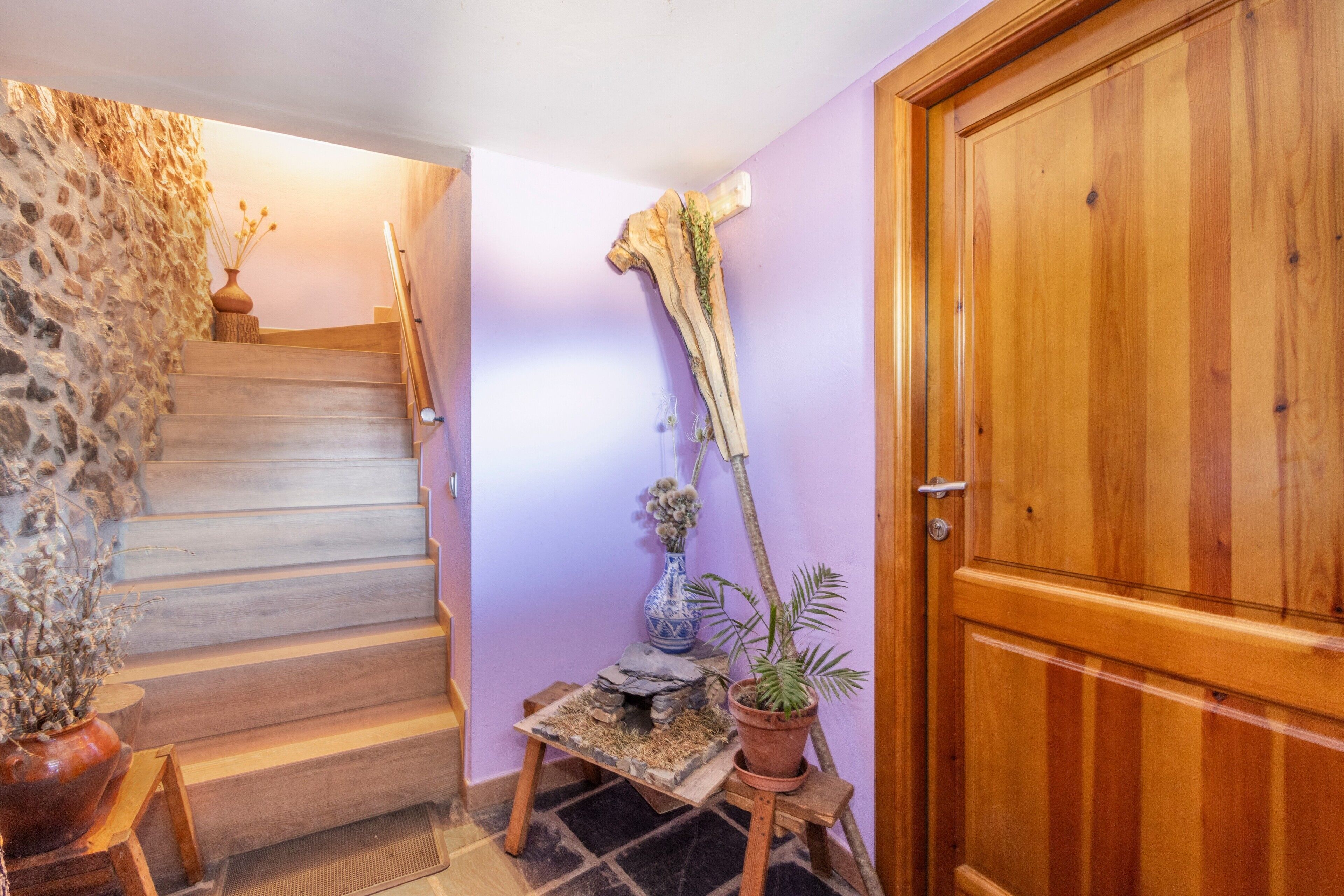 A staircase leading to a room with a wooden door, a small table with a vase and a plant, and a decorative piece on the wall.