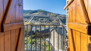 Ein Holzbalkon mit Metallgeländer, der auf eine gebirgige Landschaft blickt.