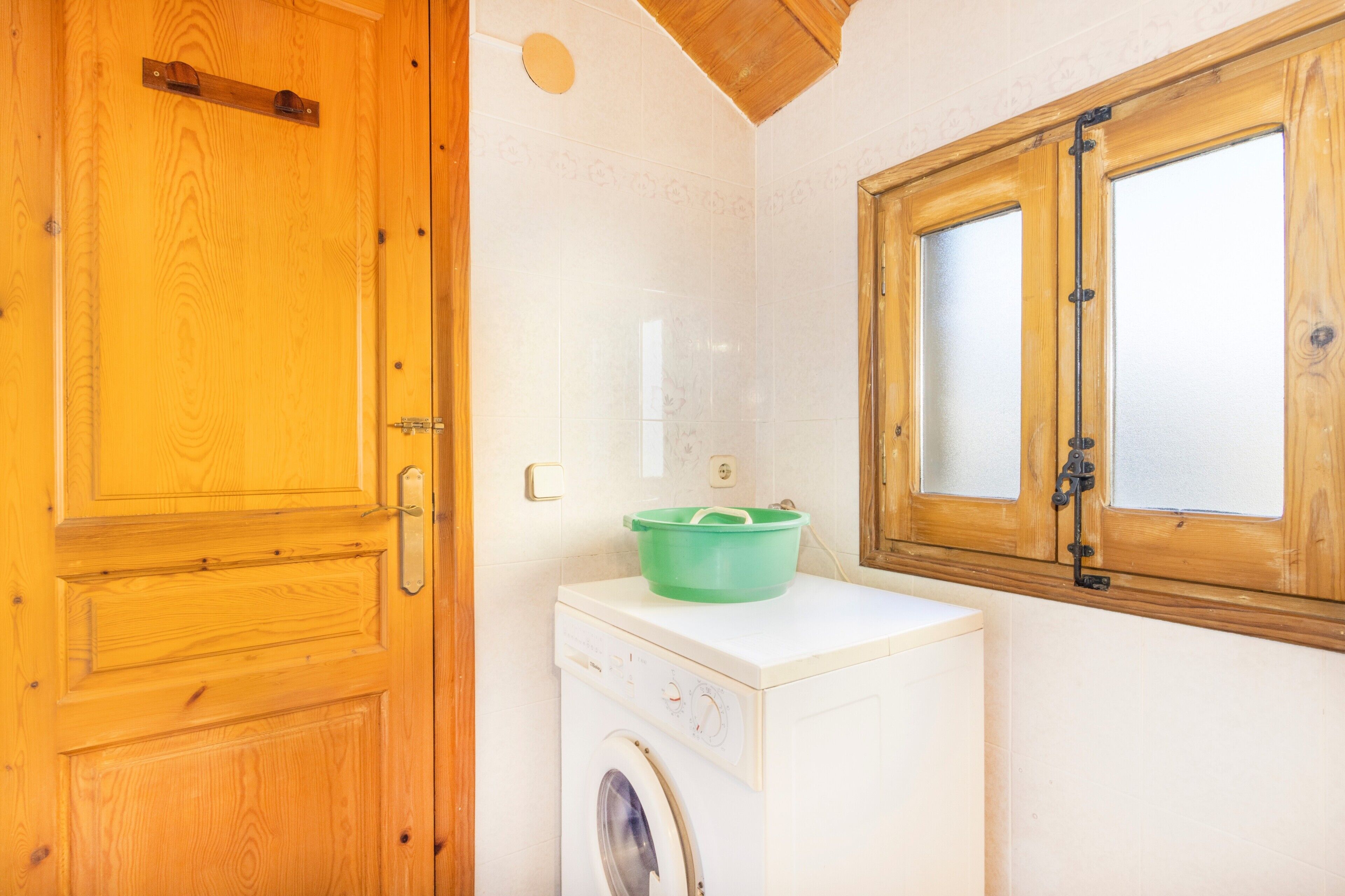 Un área de lavandería con lavadora, un lavabo verde, puertas de madera y una ventana.