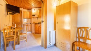 Ein Zimmer mit Holzvertäfelung, einem Esstisch, Stühlen, einem an der Wand befestigten Fernseher und einem großen Kleiderschrank.