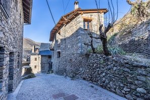 A narrow cobblestone street flanked by stone buildings with wooden balconies and a stone wall on one side.